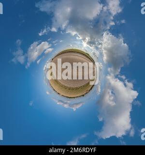 tiny planet in blue overcast sky with beautiful clouds with transformation of spherical panorama 360 degrees. Spherical abstract aerial view. Curvatur Stock Photo