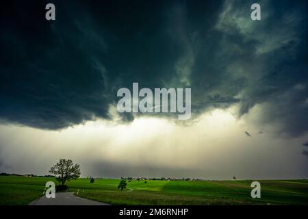 Road and meadows with thunderstorm sky in the background, Eggental, Ostallgaeu, Swabia, Bavaria, Germany Stock Photo