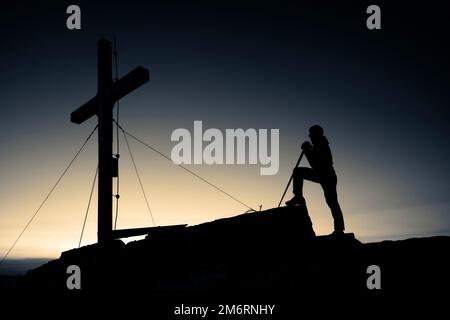 Mountaineers at the summit cross of the Namloser Wetterspitze at sunset with Lechtaler Alpen, Namlos, Reutte, Lechtal, Ausserfern, Tyrol, Austria Stock Photo