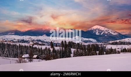 Alpine village outskirts panorama in last evening sunset sun light. Winter snowy hills and fir trees, magnificient and picturesq Stock Photo