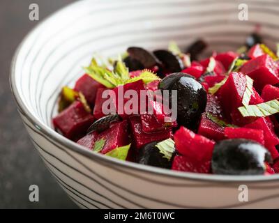 Bowl with a home made beet salad with minted beets, olives and fresh mint leaves. Stock Photo
