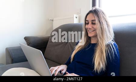 Young caucasian woman using laptop at home. Blonde woman smiling and shopping online Stock Photo