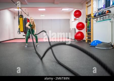 Young woman with perfect body doing crossfit exercises with a rope in the gym. Stock Photo