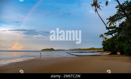 Asian women looking at a rainbow on the beach after a monsoon rain storm in Thailand Stock Photo