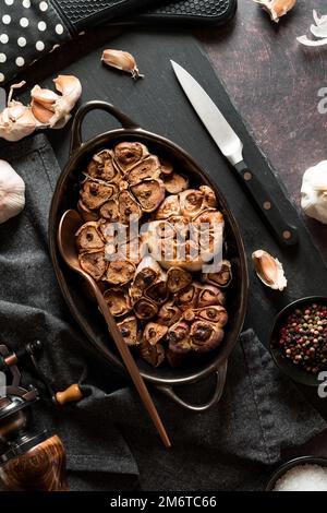 Freshly baked garlic bulbs in a roasting dish on a black slate board. Stock Photo