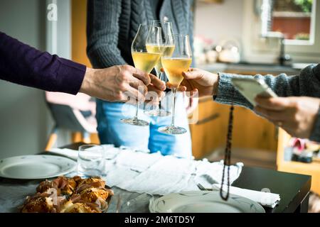 Three people celebrate Christmas by clinking glasses of prosecco at their home celebration dinner. Stock Photo