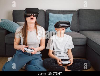 Caucasian girl and her young brother having fun at home, playing driving simulation video games by using virtual reality headsets and controllers Stock Photo