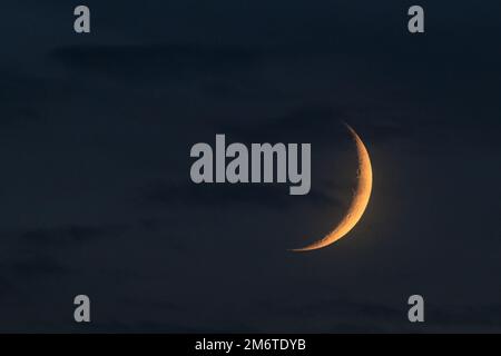 Isolated young moon crescent highlighted by sun at the evening time. On blue cloudy sky background. Astronomical photography Stock Photo