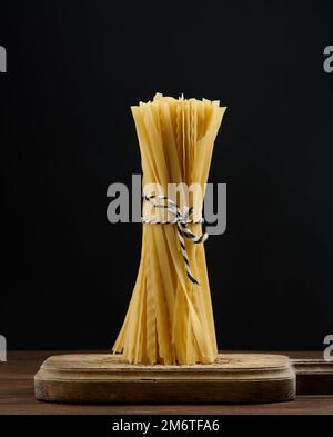 A bunch of fresh noodles tied with a rope on a brown wooden board, black background Stock Photo