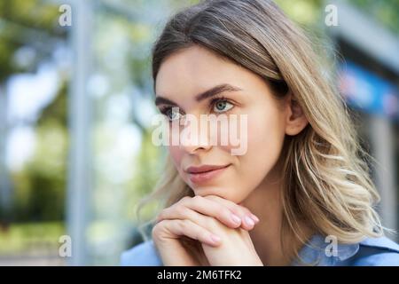 Close up portrait of young woman, looking hopeful and smiling, lean head on hands, thinking, sitting outdoors Stock Photo