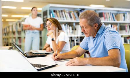 View on a mature man and a young latina student studying together Stock Photo