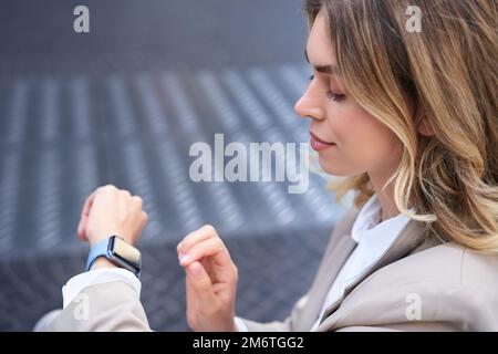 Close up portrait of business woman looking at her wrist digital watch, reading message, using app, standing outdoors in city ce Stock Photo