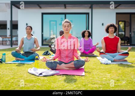 Diverse friends practicing yoga and meditating in garden Stock Photo