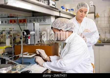 Latin male scientist using microscope while female chemist taking notes in lab Stock Photo
