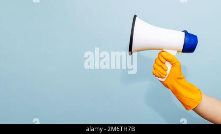 Hand in yellow protective rubber glove with megaphone on blue background Stock Photo