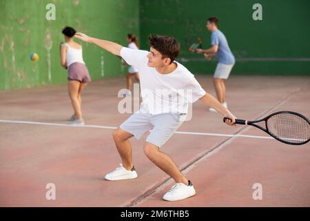 Young hispanic frontenis player swinging racquet to hit ball on outdoor court Stock Photo