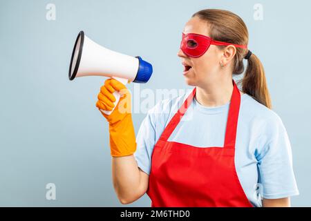 Woman in red mask, gloves and apron with megaphone on blue background Stock Photo