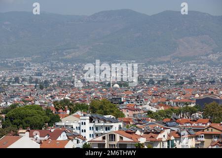 A view of the city from above against a background of towering mountains and hills. Panorama of the Turkish city of Fethiye with mosques and minarets. Stock Photo