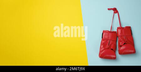 Red leather boxing gloves hanging on a cord, blue background. Sports equipment Stock Photo