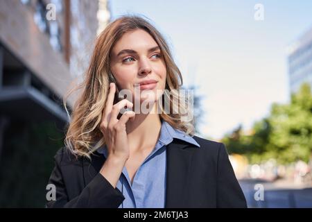 Close up portrait of smiling saleswoman, successful female manager having phone call, answer telephone and walking on street Stock Photo