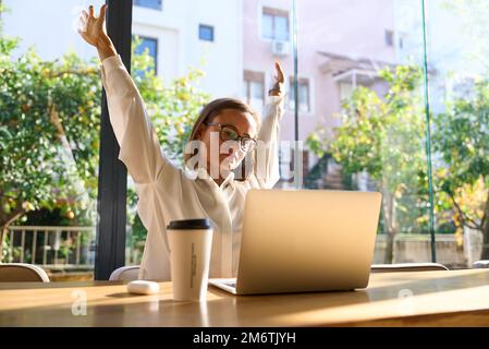 Exhausted businesswoman stretching with arms raised while working in coworking office. Stock Photo