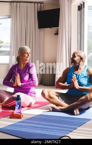 Happy senior diverse couple practicing yoga and talking Stock Photo