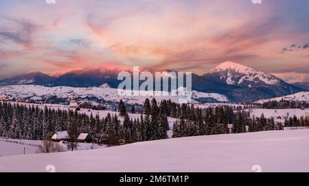 Alpine village outskirts panorama in last evening sunset sun light. Winter snowy hills and fir trees, magnificient and picturesq Stock Photo