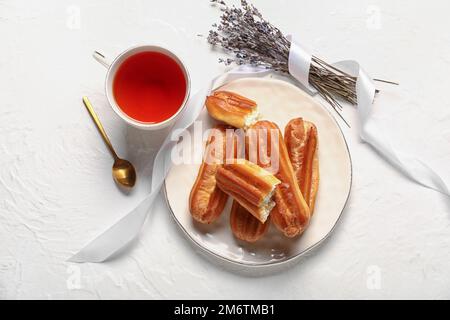 Composition with cup of tea, tasty eclairs and lavender on light background Stock Photo