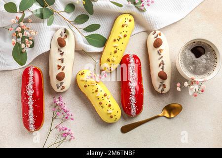 Delicious glazed eclairs, cup of coffee and floral decor on grey background Stock Photo