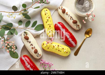 Delicious glazed eclairs, cup of coffee and floral decor on grey background Stock Photo