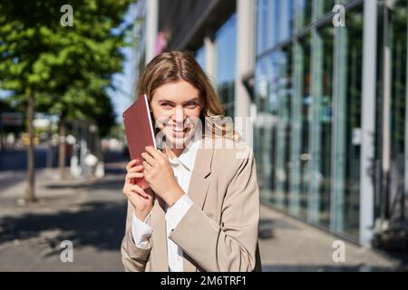 Portrait of happy businesswoman smiling, holding digital tablet on street near office building Stock Photo