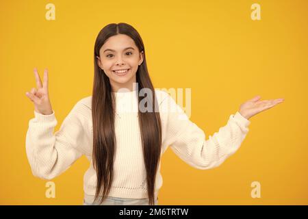 Look at advert. Teenager child points aside shows blank copy space for text promo idea presentation, poses against yellow background. Stock Photo