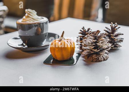 Pumpkin spice latte concept. Decorative pumpkin and cones next to hot drink with whipped cream on a table. High quality photo Stock Photo