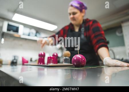 Pastry chef kitchen interior. Decorating process. Caucasian woman covering cupcakes and pralines in pink icing. High quality photo Stock Photo