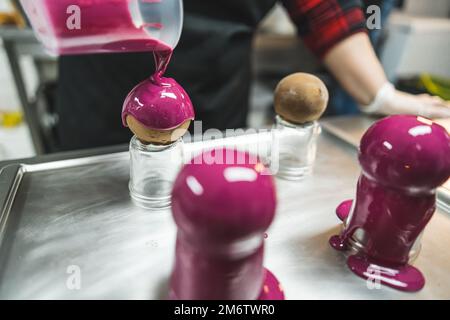 Round cakes put on small glass jars being decorated with pink glaze on a metal baking tray. Blurred background. . High quality photo Stock Photo