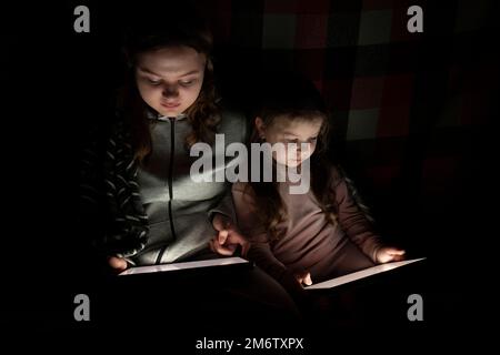 https://l450v.alamy.com/450v/2m6txpx/two-girls-use-a-tablet-pc-in-a-dark-room-blackout-energy-crisis-destruction-of-infrastructure-power-outage-concept-2m6txpx.jpg