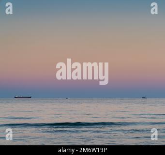 Sunset on the Black Sea off the Bulgarian coast with a fishing boat and a freight ship on the horizon Stock Photo