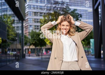 Stylish corporate woman, young lady boss in suit, looking confident and happy, posing outdoors on street Stock Photo