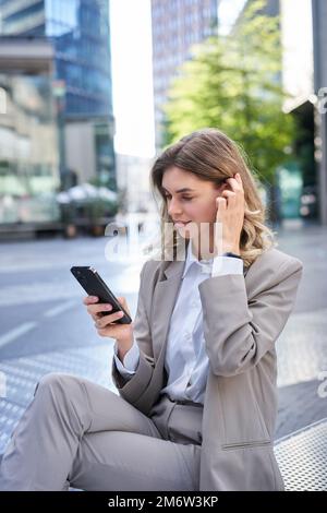 Vertical portrait of woman in suit using mobile phone, reading message or checking app, posing outdoors Stock Photo