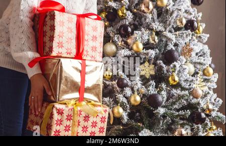Woman with stack of Christmas gifts near xmas tree at home Stock Photo