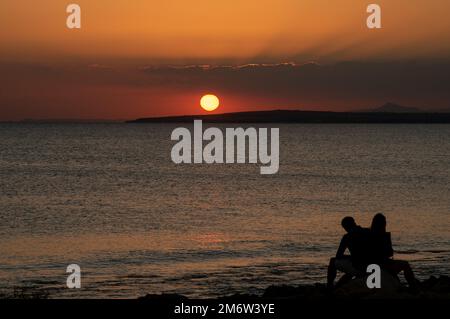 Silhouette of young couple enjoying beautiful sunset at the beach. Romantic moment human relationship Stock Photo