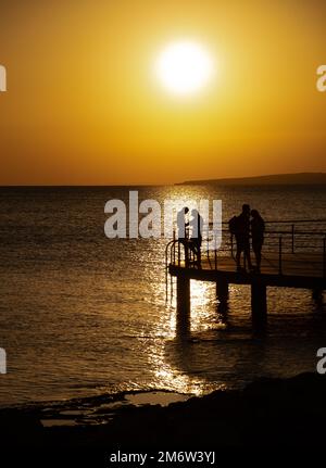 Silhouette of young couple enjoying beautiful sunset at beach. Romantic moment human relationship Stock Photo