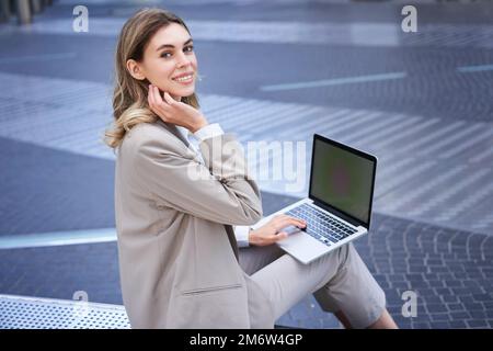Young digital nomad, businesswoman sitting with laptop in city centre. Office worker using computer outdoors Stock Photo