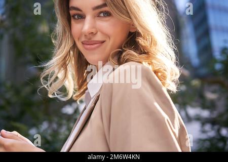Close up portrait of successful young woman, corporate lady in suit, holds her mobile phone, turns at camera with happy smile, s Stock Photo
