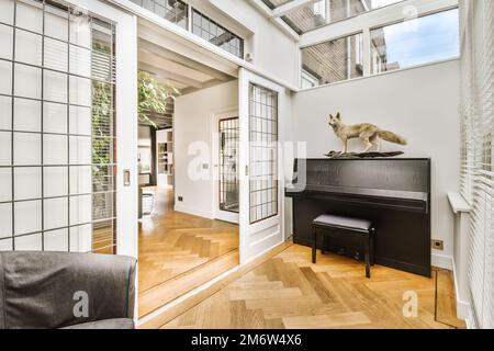 a cat sitting on top of a piano in a living room with wood flooring and white brick wall behind it Stock Photo