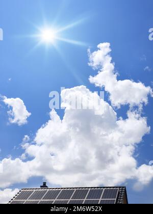 Roof with solar panels and the blue sky with clouds and sun Stock Photo
