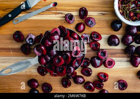 Halved and Pitted Cherries on a Wood Cutting Board: Raw cherries with tools to slice and pit them viewed from above Stock Photo