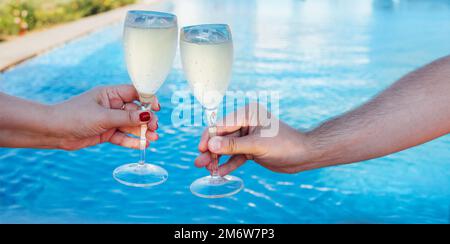 Couple holding glasses of champagne making a toast by the pool Stock Photo