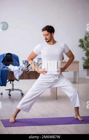 Young male employee doing sport exercises in the office Stock Photo
