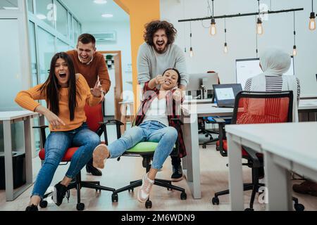Team building and office fun. Young cheerful businesspeople in smart casual wear having fun while racing on office chairs and sm Stock Photo